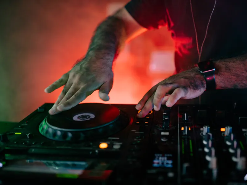 Close-up of a DJ's hands on the decks, lit red.