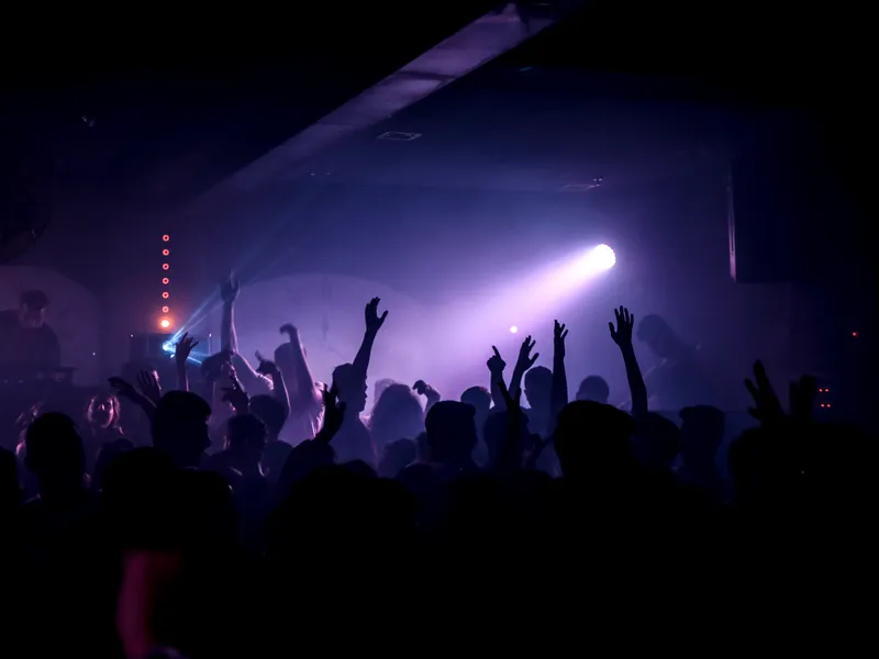 Hands raised in a dark, smoky room lit by one violet spotlight.