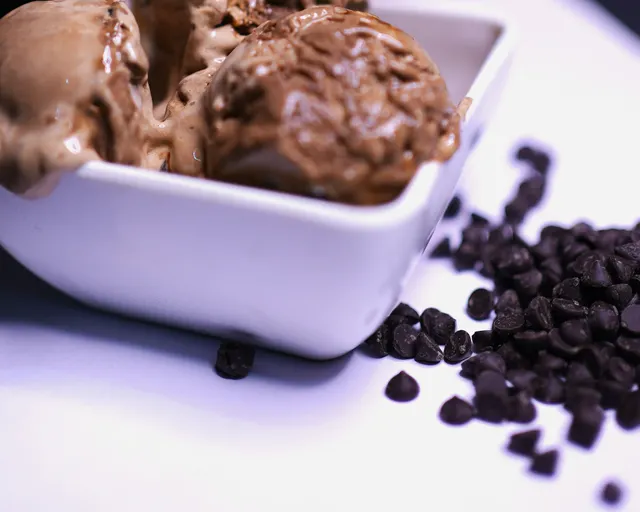 Scoops of dark chocolate in a white dish, with chocolate chips scattered beside it.