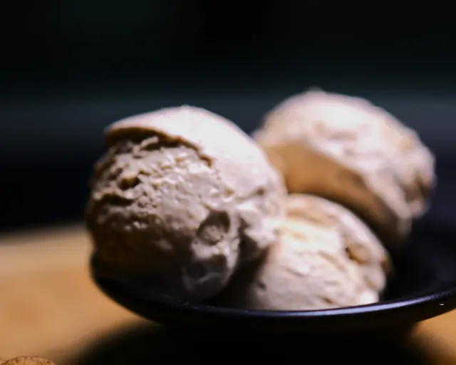 Three scoops of light brown, cinnamon-colored ice cream in a dark bowl.