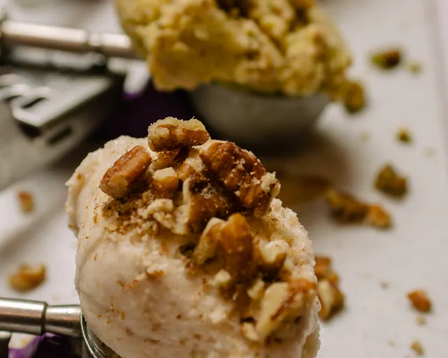 A scoop of pale maple ice cream piled with candied walnuts.