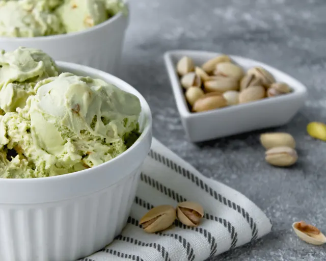 Pale green pistachio ice cream in white bowls, with a dish of shelled pistachios.