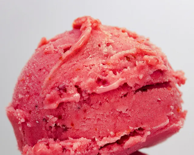 A close-up of a bright pink strawberry scoop with visible fruit.