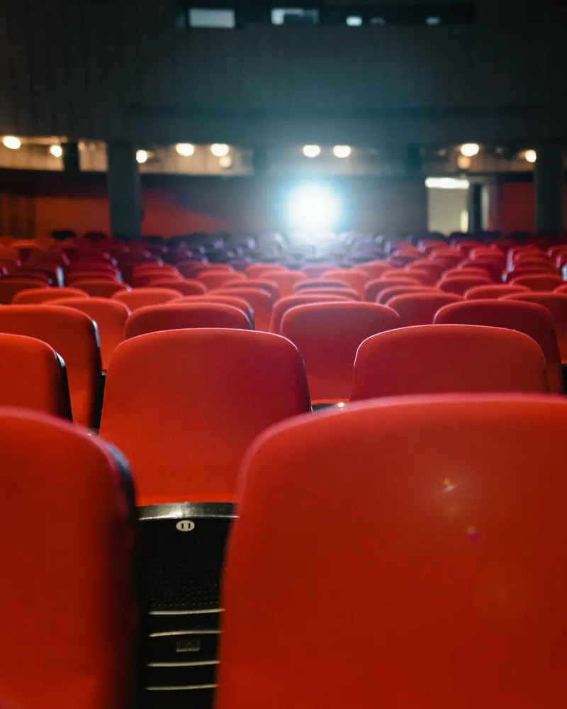 A view of an empty cinema with rows of red seats facing the illuminated screen.
