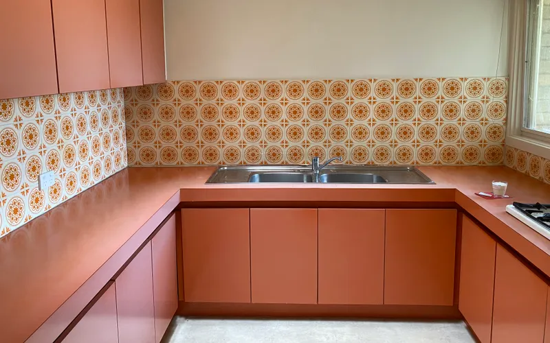 A 1970s kitchen with patterned orange wall tiles and a steel sink, in flat daylight.
